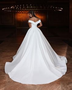 a woman in a white wedding dress is looking down at the floor with lights behind her