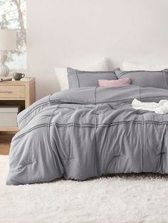 a bed with grey sheets and pillows on top of white fluffy carpeted flooring