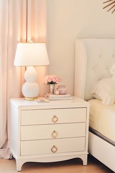 a white nightstand with flowers on it next to a bed