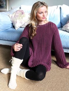 a woman is sitting on the floor with her legs crossed wearing socks and a sweater