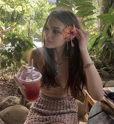 a woman sitting on a bench holding a drink and looking at the camera with her hand in her hair