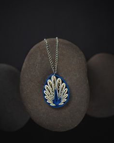 a blue and white peacock pendant sitting on top of a black rock next to some rocks