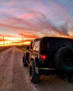 a jeep parked on the side of a dirt road at sunset with power lines in the background