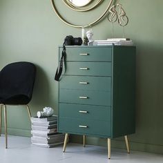 a green chest of drawers next to a black chair and round mirror on the wall