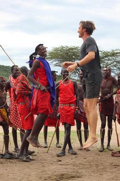 a man standing in front of a group of people wearing red and blue outfits with sticks