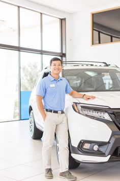 a man standing next to a white honda car in a dealership with his hands on the hood