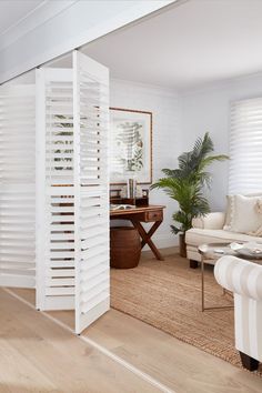 a living room with white shutters on the walls and wood flooring in it