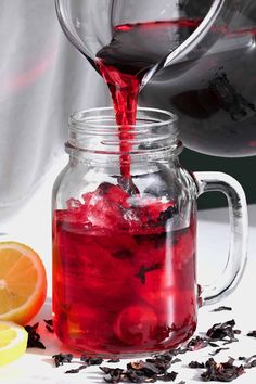 red liquid being poured into a mason jar filled with tea leaves and orange slices on a white surface