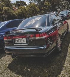 the rear end of a black car parked on grass next to other cars in a parking lot