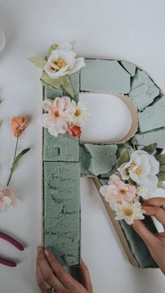 two hands are working on the letters made out of wood and paper flowers with scissors