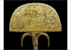 an ancient gold object with horses and carriages on it's back end, against a black background