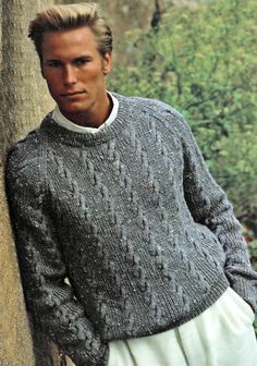 a man leaning against a tree wearing a sweater