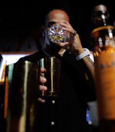 a man holding a glass in front of his face while standing next to other bottles