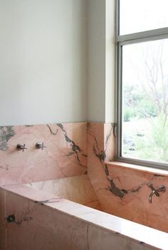 a bath tub sitting next to a window in a room with marble walls and floors