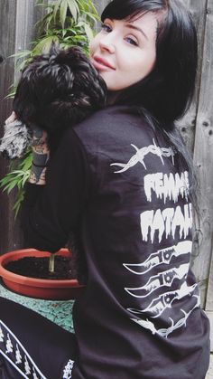 a woman sitting next to a potted plant holding a black dog in her lap