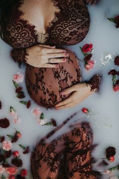 a pregnant woman laying in a bathtub with flowers all over her body and hands on her stomach