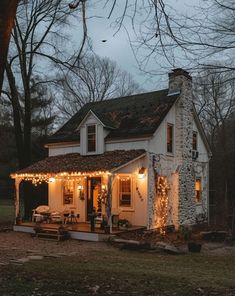 a white house with christmas lights on the front porch and covered porch area, surrounded by trees