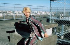 a man with blonde hair is standing on some stairs in front of a fence and looking off into the distance