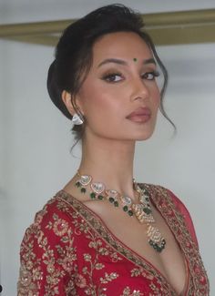 a woman in a red sari with jewelry on her neck and chest is looking off to the side