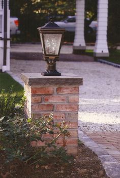 an old fashioned street light on top of a brick pillar in front of a house