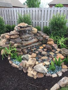 a garden with rocks and plants in the center, along with a water feature surrounded by mulch