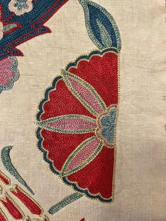 an embroidered piece of cloth with flowers and leaves on the front, in red, blue, pink and white colors