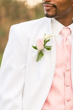 a man in a white suit and pink tie with a flower on his lapel