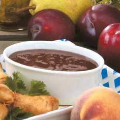 there is a bowl of chocolate sauce next to some apples and other fruit on the table