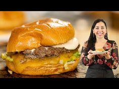 a woman standing next to a large hamburger on a table with a plate in front of her