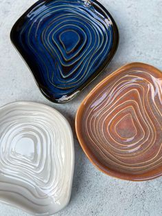 three ceramic bowls sitting on top of a white floor next to each other in different shapes and sizes