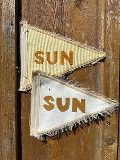 two pennants with the word sun on them hanging from a wooden door, next to each other