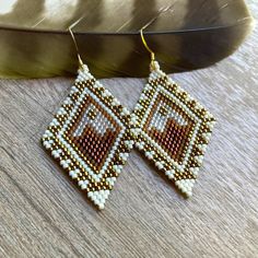 a pair of beaded earrings sitting on top of a wooden table next to a feather