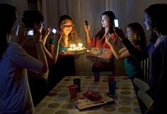 a group of people standing around a table holding up cell phones with candles in them