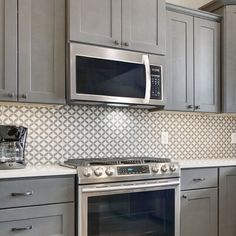 a stainless steel oven and microwave in a kitchen with gray cabinets, white counter tops and grey cupboards