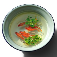 three small fish in a bowl with water and green sprouts on the side