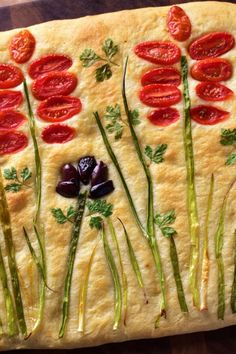 an artful pizza with tomatoes and asparagus on it, sitting on a wooden table