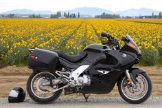 a black motorcycle parked in front of a field of yellow flowers