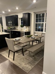 a dining room table and chairs in a kitchen with black cabinets, white walls and wood flooring