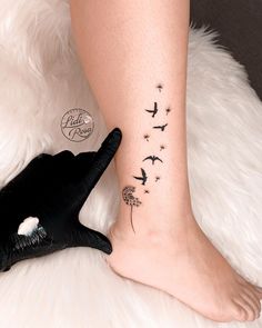 a woman's foot with a dandelion tattoo on her left ankle and black birds flying above it