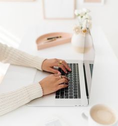 a woman is typing on her laptop while sitting at a desk with a cup of coffee