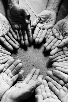 many hands are arranged in the shape of a circle on a wooden table with their fingers together