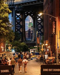 people are walking down the street in front of a bridge