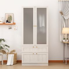 a white cabinet sitting in the corner of a room next to a lamp and potted plant