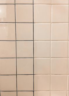 a white tiled wall with black grouting on the bottom and one line in the middle