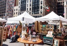 an outdoor flea market in the city with lots of tables and umbrellas set up