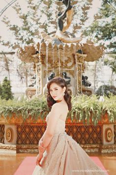 a woman in a wedding dress standing on a red carpet with a fountain behind her