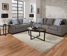 a living room with two couches and a coffee table in front of a brick wall