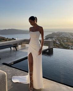 a woman in a white dress standing on the edge of a pool with her legs crossed