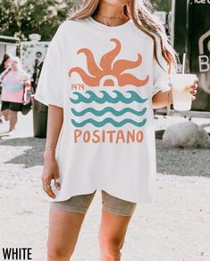 Embrace the coastal charm of Italy with this vintage-inspired Positano tee! Featuring a sun and wave graphic, this shirt captures the nostalgic allure of seaside escapes and timeless summer vibes. Want a different location or year printed on your t-shirt? Simply enter your request in the personalization box prior to checkout. If no personalization is requested, your shirt will be printed as show in the images.  We use professional quality DGT printing on all our apparel. Direct-to-garment, or DT White Shirt With Front Print For Summer, White Beachy Tops With Screen Print, White Beachy Top With Screen Print, Beachy White Top With Screen Print, White Printed Beachy Tops, Beachy White Printed Tops, White Crew Neck Summer Shirt, Beachy White Short Sleeve Tops, White Short Sleeve Beachy Tops