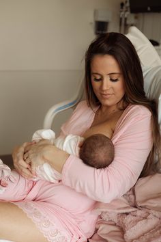 a woman holding a baby in her arms while sitting on a bed with pink sheets